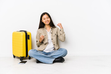 Young chinese traveler woman sitting holding a boarding passes raising fist after a victory, winner concept.