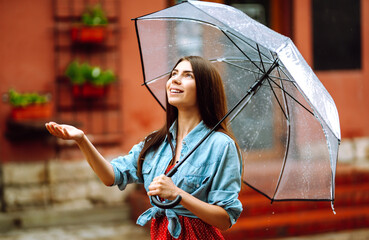 Cheerful woman  under a transparent umbrella enjoying rainfall. Young woman hiding from the rain....
