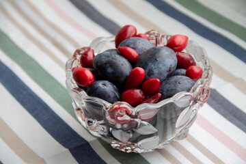 plums and red dogwood berries in a glass vase