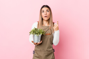 Young gardener woman holding a plant pointing upside with opened mouth.