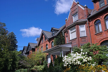 Street of old semi-detached houses with gables and summer flowers in lush gardens