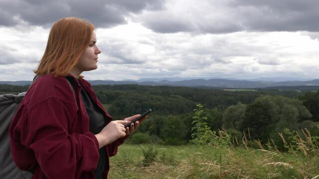 teenage girl without makeup stands against mountains with mobile phone