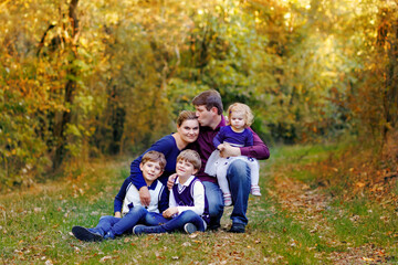 Naklejka na ściany i meble Portrait of young parents with three children. Mother, father, two kids brothers boys and little cute toddler sister girl having fun together in autumn forest. Happy family of five