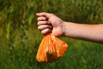 An image of an out stretched hand holding a orange plastic dog poop bag full of dog poop and ready for disposal. 