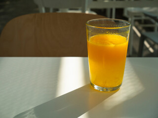 Glass of freshly squeezed orange juice on white table, school setting, liquid orange extract full of vitamin c