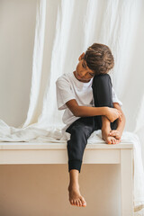 Tired indian asian kid sitting on a table, hugging his leg