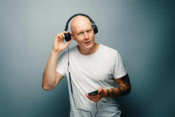Young handsome emotional bald man with headphones opens one ear trying to hear someone trough the loud music.
