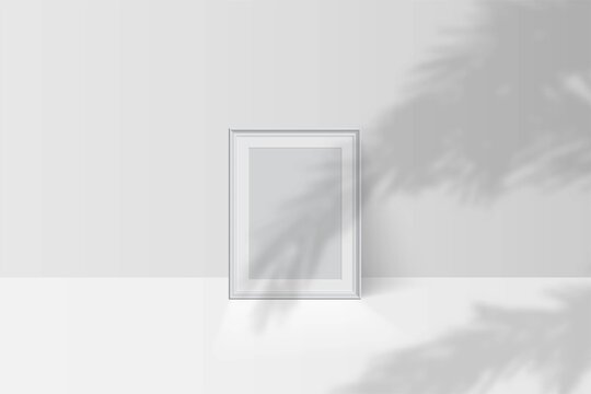 Tropical palm leaf shadow falls on blank vertical white picture frame