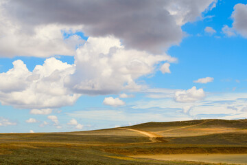 Landscape. Sky with clouds over hills and fields. On the field there is a dirt road going up.