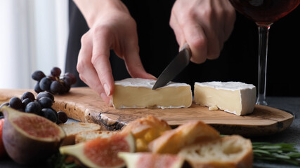 Preparing cheese plate with soft camembert cheese, figs and grapes. Woman's hands slicing cheese