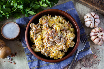 Lunch is hearty: stewed potatoes with mushrooms and fresh herbs in a clay plate on a gray background. The view from the top
