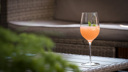 Orange Aperitif with mint standing on an outdoor table, a garden lounge and plants in the...