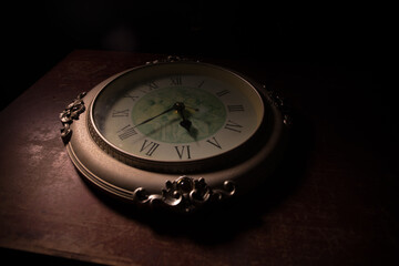 Time concept. Big vintage round clock on wooden table with abstract light.