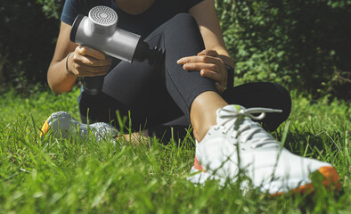 Woman massaging leg with massage percussion device after workout.