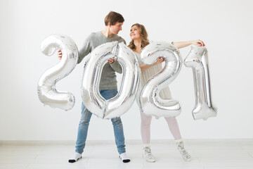 Holidays, festive and party concept - Happy loving couple holds silver 2021 balloons on white background. New Year celebration.