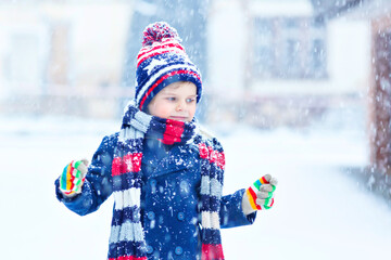 Cute little funny child in colorful winter fashion clothes having fun and playing with snow, outdoors during snowfall. Active outdoors leisure with children. Kid boy and toddler catching snowflakes.