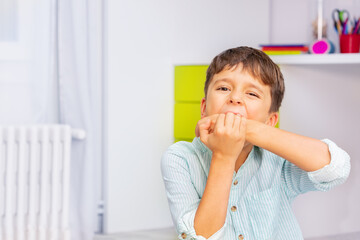 Close portrait of little autistic boy bite hands with strong negative face expression sitting in...
