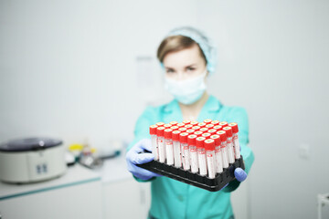 A woman nurse doctor in a medical mask holds test tubes for a blood test