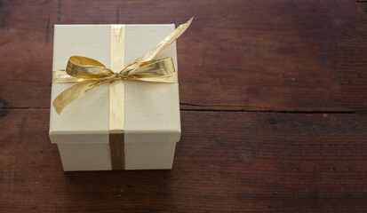 Beige closed gift box with gold color ribbon on wooden table