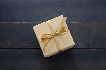 Beige closed gift box with gold color ribbon on blue table background
