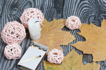 Candle stub on brushed pine boards. Nearby are dried maple leaves and rattan balls.