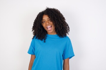 Young african woman with curly hair wearing casual blue shirt over white background winking looking...