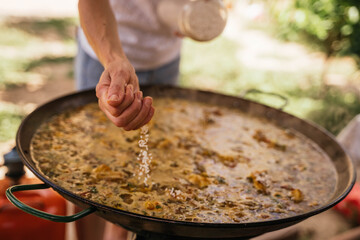 Young Spanish woman pouring rice into the paella pan during the preparation of the typical Spanish seafood paella