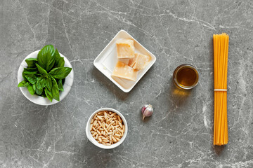 Fototapeta na wymiar Pasta with pesto ingredients. Top view of spaghetti, basil, pine nuts, garlic, parmesan and olive oil on gray stone background