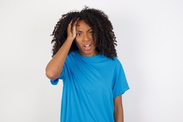 Embarrassed attractive Young african woman with curly hair wearing casual blue shirt, with shocked expression, expresses great amazement, Puzzled woman poses indoor