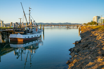 Fototapeta premium Waterfront at Fisherman's Wharf with moored commercial fishing boat and city downtown with railway bridge in distance.