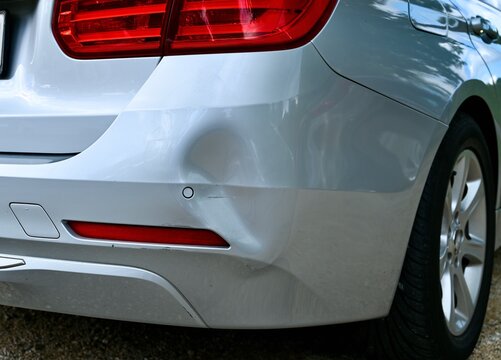 Backside of car has dented rear bumper damaged after accident in the parking lot.