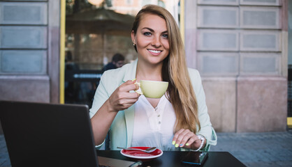 Happy woman with cup of coffee and laptop in cafe