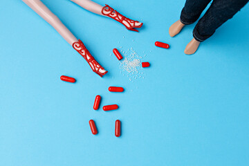 Dolls legs in heels with floor full of red pills with men legs staying beside. Pills over usage and addiction minimal concept.