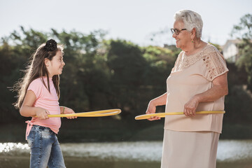 Grandmother playing hula hoop with her grandchildren outdoors.