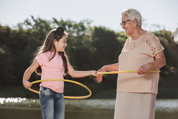 Grandmother playing hula hoop with her grandchildren outdoors.
