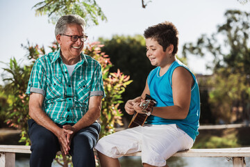 Grandfather and grandson singing and playing ukulele.