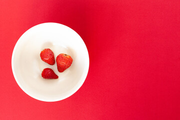 three red strawberries on a white plate on the red background, isolated
