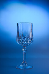 Wineglass on the light background. Fine cristal glassware concept. Vertical, toned in blue