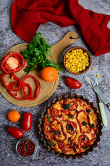 Top view of colorful baked vegetables, corn and a cutting board with red bell peppers on a rustic background.