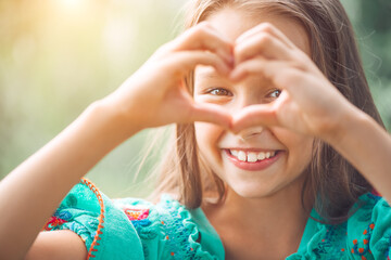 Cute child girl showing heart gesture and smiling outdoor. Love summer. Beautiful seven years old...