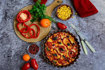 Colorful baked vegetables, tomatoes, corn and a cutting board with red bell peppers on a gray background. Top view