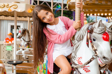 Fototapeta na wymiar A teenage girl with long hair rolls around on a swing horse carousel. Sitting on a horse at an amusement park