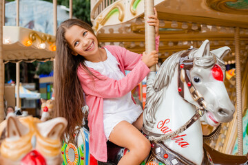 A teenage girl with long hair rolls around on a swing horse carousel. Sitting on a horse at an...