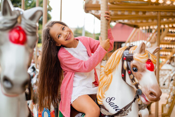 A teenage girl with long hair rolls around on a swing horse carousel. Sitting on a horse at an...
