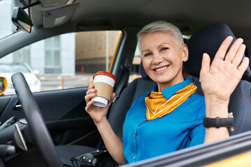 Confident cheerful mature businesswoman with short blonde hair sitting in driver's sear holding...