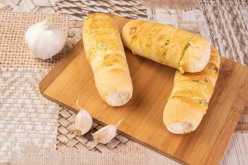 Garlic bread stuffed with cheese arranged on a cutting board with garlic around it, on a table, selective focus.