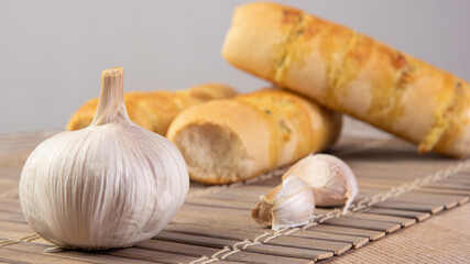 Garlic bread stuffed with cheese arranged on a bamboo mat with garlic around it on a table, selective focus.