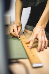 Selective focus of seamstress making layout with ruler and soap on green cloth on wooden table 