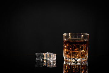 Empty glass for whiskey, cognac or bourbon next to it is scattered ice, old type of fashion, copy space, selective focus, there is a place to write text