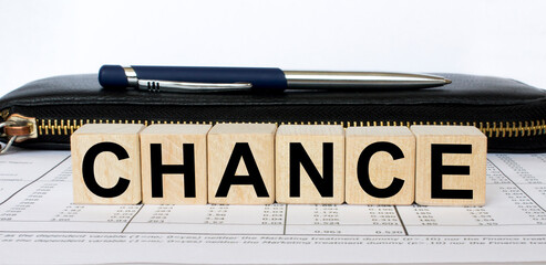 A word Chance written in a wooden cube with a pen and wallet